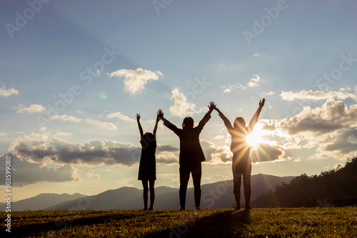 family silhouette with raised arms looking at sunset. Backlight shot. success, friendship and community concepts.