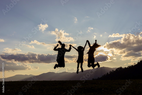 family silhouette jumping with raised arms at sunset. Backlight shot. success, friendship and community concepts.