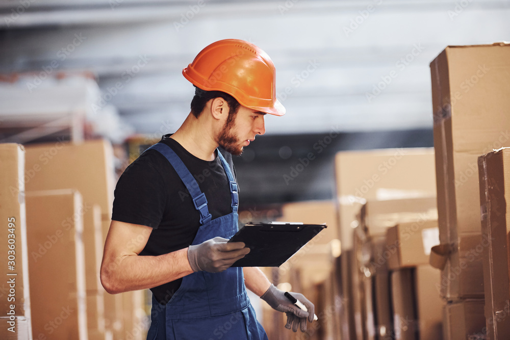 Fototapeta premium Storage worker in uniform and notepad in hands checks production