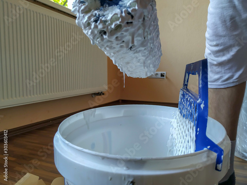 Man holding paint roller, filling it with white color for repainting and renovating the house professionally
