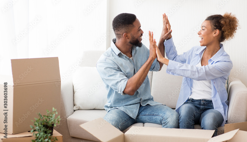 Happy Afro Spouses Giving High-Five Sitting Among Moving Boxes Indoor Happy Afro Spouses Giving High-Five Sitting Among Moving Boxes Indoor