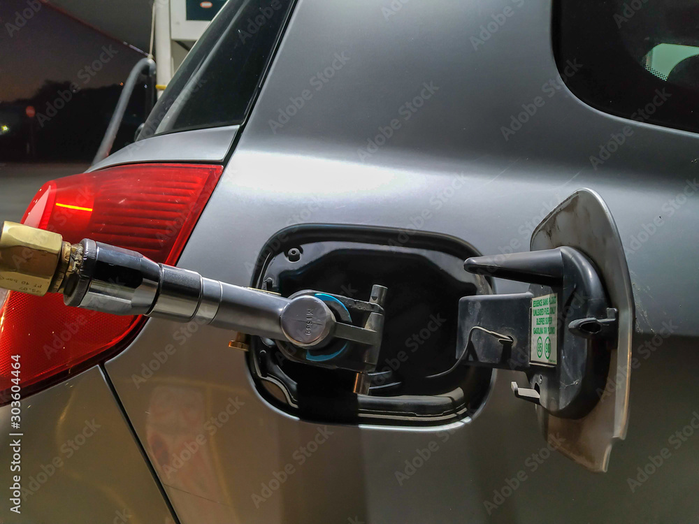 Gas hose pumping gas into grey car during nighttime travel. Refilling gas for extra energy and power