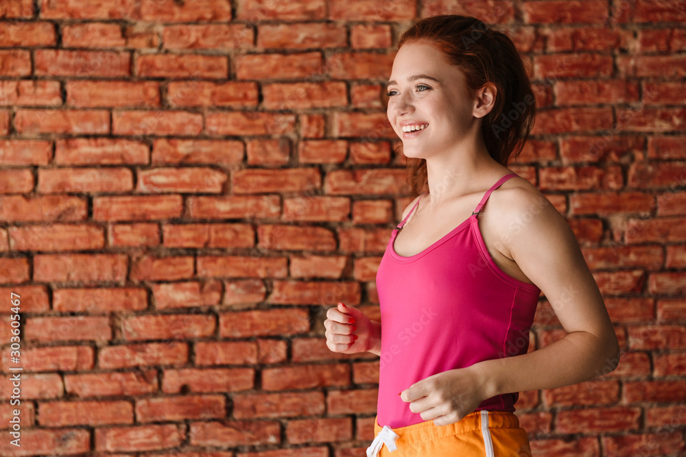 Redhead fitness woman posing over brick wall background.