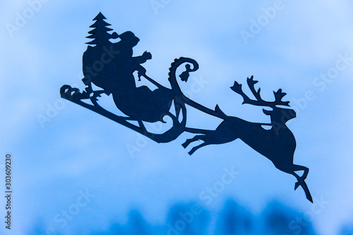 Christmas decorations made of paper on the window glass, Santa Claus in a sleigh on a deer