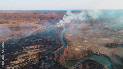 Black burned field  a bush burns in the distance and there is a strong thick smoke. A small river blocks the path of fire.