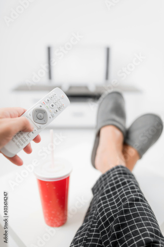 Man drinking soda juice and looking at TV with legs on the table in living room. photo