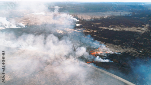 Forest and field fire. Dry grass burns  natural disaster. Aerial view. Smooth flight over the place of fire  a small stream blocks the path to the fire.