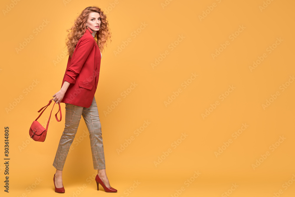 Fashionable woman in Trendy red outfit, stylish wavy hair, makeup. Joyful lady in jacket smiling dance on orange. Cheerful girl, stylish fashion red heels, accessories, beauty style Fashionable woman in Trendy red outfit, stylish wavy hair, makeup. Joyful lady in jacket smiling dance on orange. Cheerful girl, stylish fashion red heels, accessories, beauty style