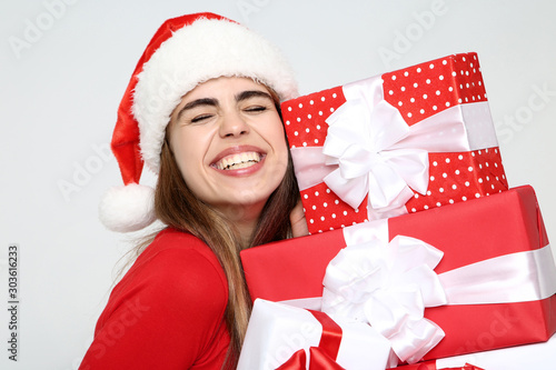 Beautiful woman wearing santa hat and holding gift boxes on grey background