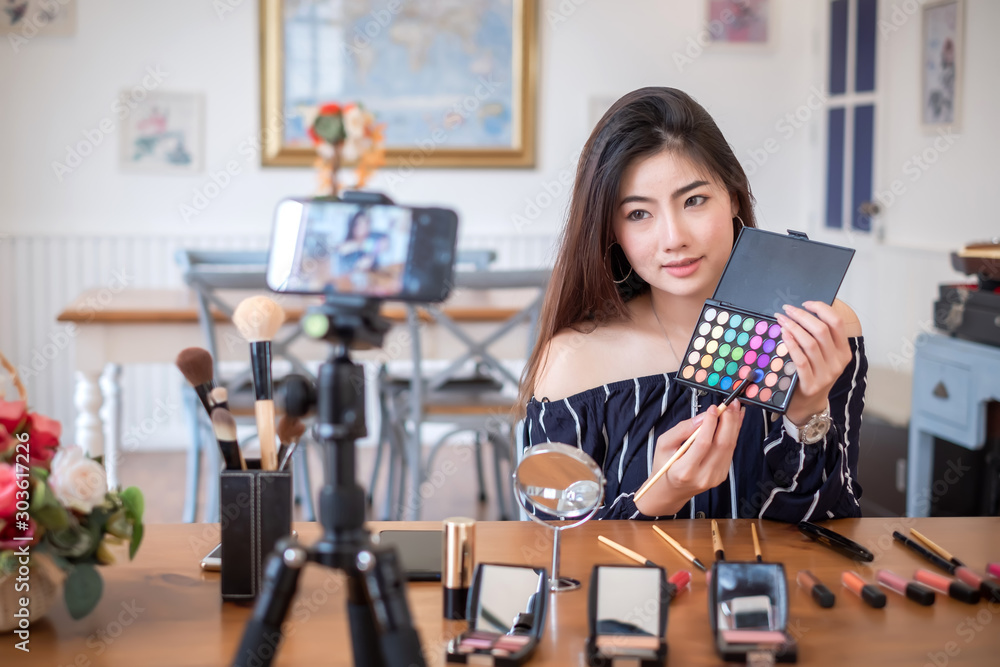 Asian woman blogger with makeup cosmetics recording video clip by smartphone at home.