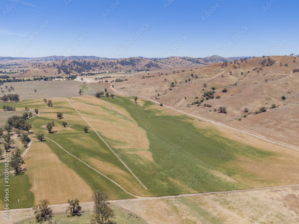 Fototapeta premium Panoramic high angle aerial drone view of rural New South Wales, Australia, near the town of Gundagai on a sunny day. Gentle hills, a country road and agricultural fields near Tumut River.