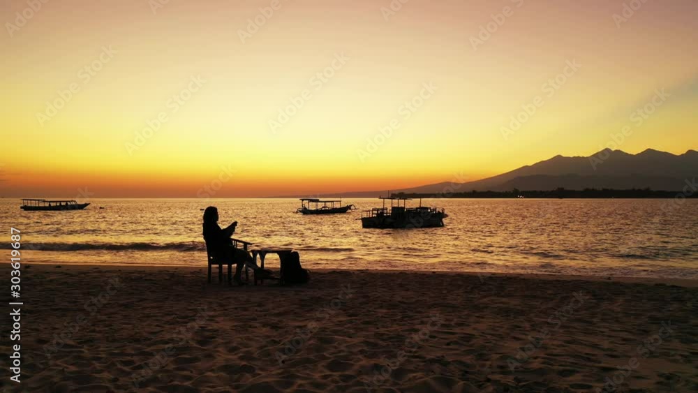 Thoughtful girl enjoying glowing orange sky after sunset on quiet beach washed by calm lagoon with anchored boats in Malaysia Thoughtful girl enjoying glowing orange sky after sunset on quiet beach washed by calm lagoon with anchored boats in Malaysia