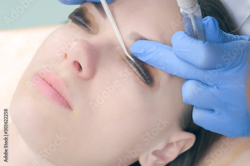Beautician bending lashes with needle into curlers  lift eyelashes laminaton procedure in beauty salon for woman  face closeup. Cosmetologist making lash lifting in cosmetology clinic  hands closeup.
