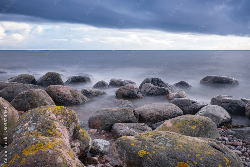 Boulders, forest, shore, evening light, sunset, clouds, blue sky and rainbow on the Baltic Sea. Mohni, small island in Estonia, Europe.