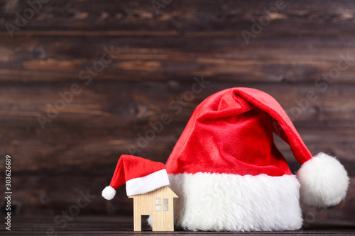 Red santa hats with house model on brown wooden background