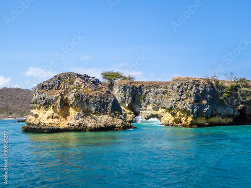 A cliff formation emerging from the calm sea. The water has many shades of turquoise. Sunny and cloudless day. Unspoiled and raw beaches of Indonesia. Hidden gem.