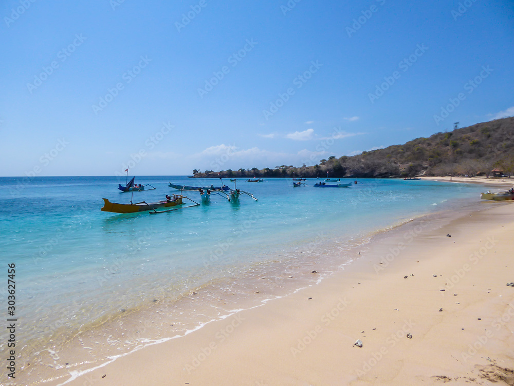 A view on an idyllic Pink Beach on Lombok, Indonesia. Many boats drifting on a calm surface of the sea, some anchored to the shore. Unspoiled, hidden gem. Perfect place for peaceful, relaxed holidays