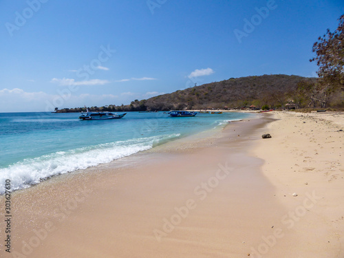 Fototapeta Naklejka Na Ścianę i Meble -  A view on an idyllic Pink Beach on Lombok, Indonesia. Many boats drifting on a calm surface of the sea, some anchored to the shore. Unspoiled, hidden gem. Perfect place for peaceful, relaxed holidays
