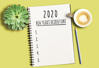 top view of notepad with text 2020 New Years Resolutions and numbered list on yellow desk with succulent plant and cup of coffee