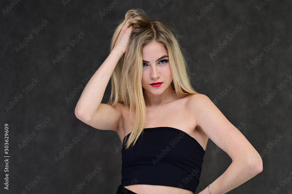Fototapeta premium The concept of fashionable glamor, cosmetics and beauty with a pretty girl. Portrait of a fashionable beautiful blonde model with long hair, great makeup, on a gray background.