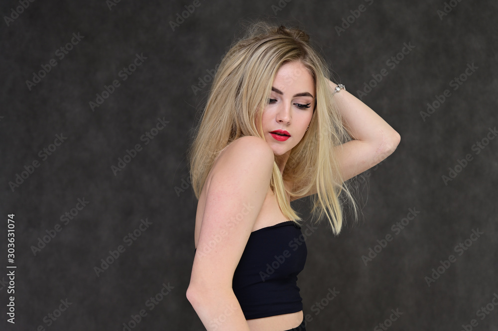 The concept of fashionable glamor, cosmetics and beauty with a pretty girl. Portrait of a fashionable beautiful blonde model with long hair, great makeup, on a gray background.