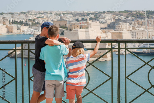 Best friends on holidays. Three kids standing together on top point of city. Malta cityscape