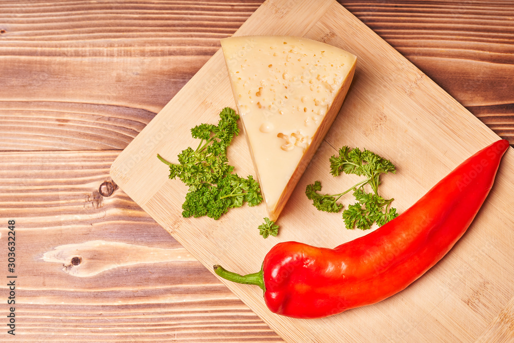 Maasdam cheese on a wooden table with herbs and red pepper Maasdam cheese on a wooden table with herbs and red pepper
