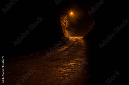 Dark road at night iluminated by a single streetlight photo