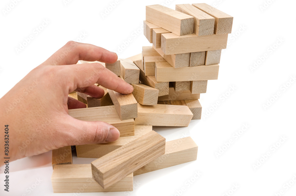 Planning, risk and strategy in business, hand gambling placing a wooden block on a tower. Wooden blocks isolated on a white background. Planning, risk and strategy in business, hand gambling placing a wooden block on a tower. Wooden blocks isolated on a white background.