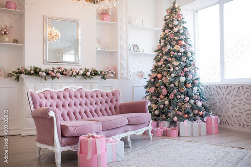 Interior of bright modern living room with fireplace and comfortable sofa decorated with Christmas tree and gifts