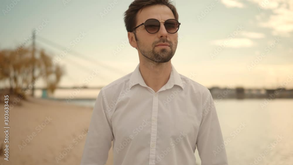 Cheerful Romantic Guy In Sunglasses Walks On Sand And Dreaming.Man Walking On City Beach.Lonely Handsome Confident Businessmen In Pants Stroll On City Sands Beach.Attractive Man Walking On Sand Beach. Cheerful Romantic Guy In Sunglasses Walks On Sand And Dreaming.Man Walking On City Beach.Lonely Handsome Confident Businessmen In Pants Stroll On City Sands Beach.Attractive Man Walking On Sand Beach.