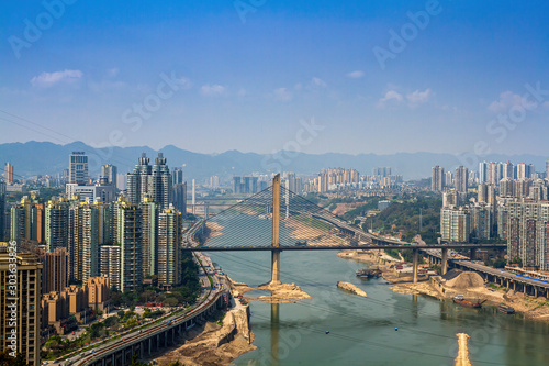 Chongqing, China - March 20, 2018: Top view of the  Jialing River in the Chinese city of Chongqing. Bridges, roads, city blocks, mountains. Sunny day. © Stepanov Aleksei