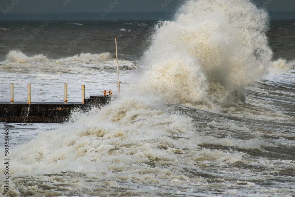 breakwater and harbour in stormy weather with huge waves crashing over the walls pier. Abnormally strong storms in the middle latitudes as a result of global warming.