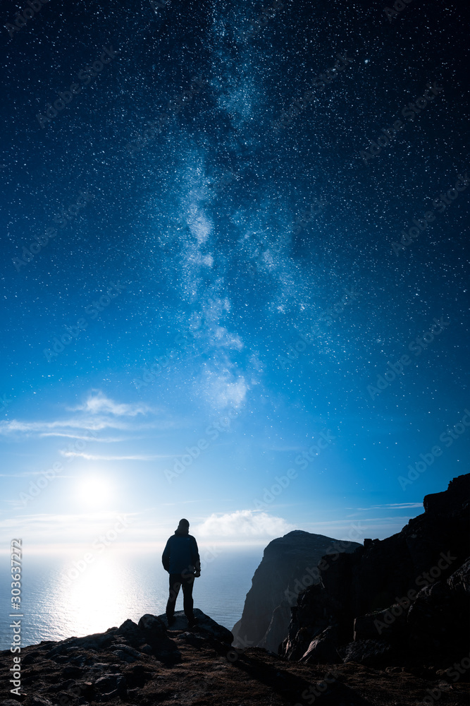 Obraz na plátně A lonely man standing by a cliff and looking at the ocean and stars of the milky