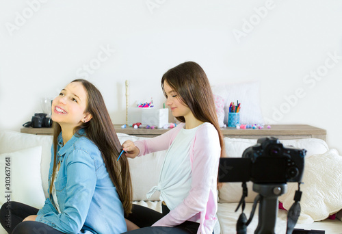 Two teen girls blogger presents beauty products, combs and curling hair and transmits live video to social networks. Focus on the influencer of teenage blogger girls. Beauty blogger and vlog concept. © Natalia