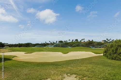 Beautiful view of process of automatic golf field and green trees on blue sky background. Tropical natural landscape backgrounds. Aruba island.Garden concept.