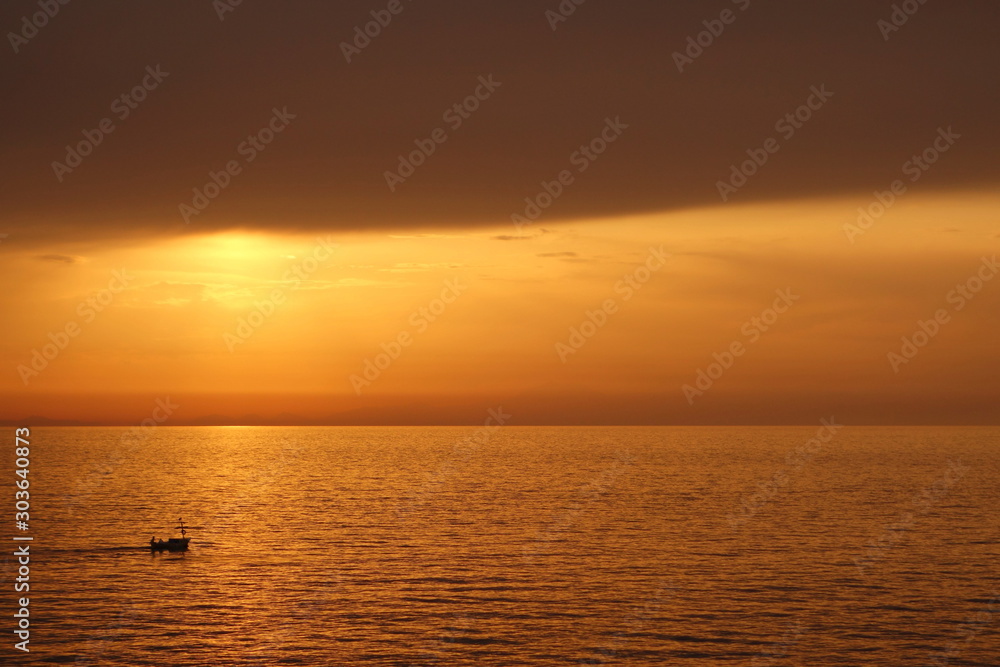 Boat in the sea at sunset to the left of the sun