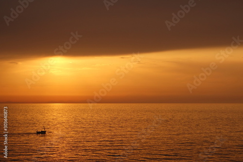 Boat in the sea at sunset to the left of the sun