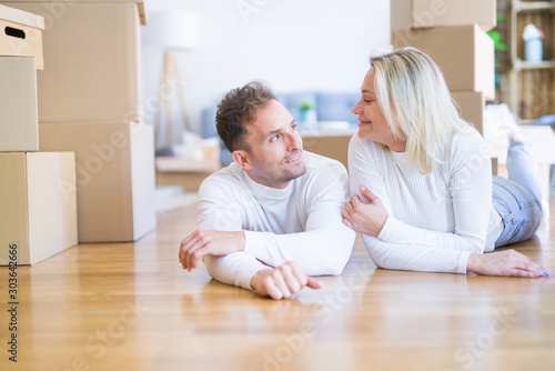 Young beautiful couple lying down on the floor at new home around cardboard boxes