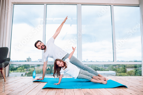 Fototapeta Naklejka Na Ścianę i Meble -  happy girl and her father doing yoga at home using yoga mats
