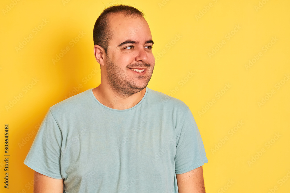 Obraz premium Young man wearing green casual t-shirt standing over isolated yellow background looking away to side with smile on face, natural expression. Laughing confident.