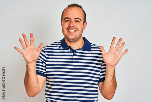 Young man wearing casual striped polo standing over isolated white background showing and pointing up with fingers number ten while smiling confident and happy.