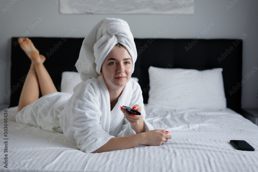 girl in a bathrobe is lying on the bed watching TV. woman resting after spa treatments. girl in a bathrobe is lying on the bed watching TV. woman resting after spa treatments.
