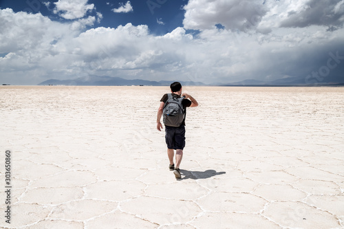 Young man walking with his backpack on the salt flats in the Salinas Grandes in Jujuy, Argentina
