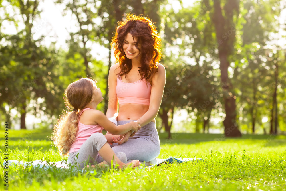 attractive woman and small girl sitting on the mat holding hands in the park at daytime attractive woman and small girl sitting on the mat holding hands in the park at daytime