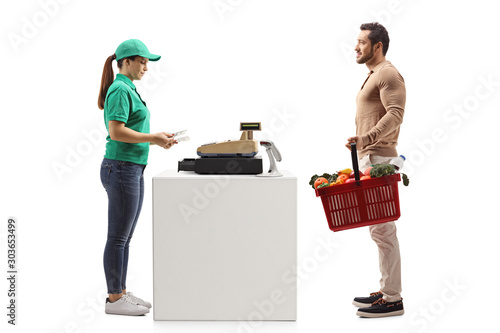 Young man with a shopping basket at a cash register paying to a female cashier