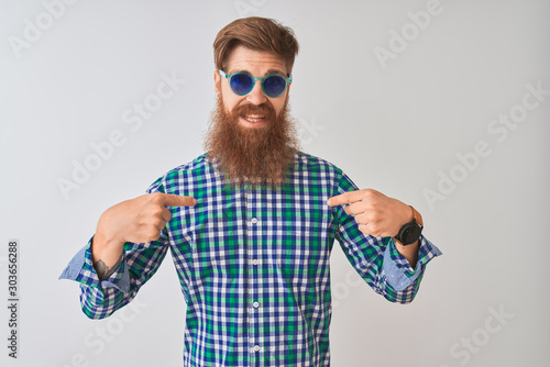 Young redhead irish man wearing casual shirt and sunglasses over isolated white background looking confident with smile on face, pointing oneself with fingers proud and happy.