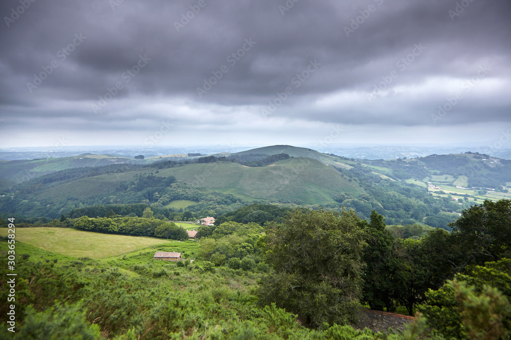Hilly rural landscape in the foothills at cloudy summer day. Atlantic Pyrenees, France. Overcast weather