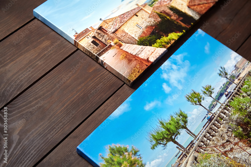 Canvas photo prints lying on a wooden table. Sample of gallery wrapping method of canvas stretching on stretcher bar. Side view of colorful photographs printed on glossy synthetic canvas - obrazy, fototapety, plakaty 