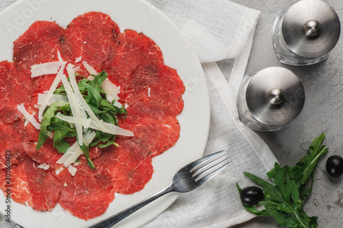 Carpaccio made of raw marbled beef, high angle view on a white plate, horizontal shot